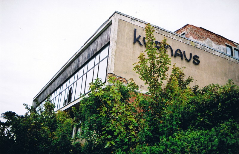 Ahrenshoop, Dorfstraße (2003). Das Kurhaus-Hotel gehörte zum Reisebüro der DDR. Zu den Gästen zählten zumeist Künstler und die so genannte „Schaffende Intelligenz.“ Das Haus besaß 21 Zimmer inklusive einer Suite sowie 60 eigene Strandkörbe. Beliebte Veranstaltungen waren die thematischen Sommernachtsbälle mit 200 Gästen. Das Haus wurde 1993 geschlossen.